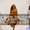 A wide banner featuring three women side-by-side against a neutral, light backdrop, modeling natural, sustainable clothing. Across the center, a dark semi-transparent overlay displays white text that reads, "Stop Buying Toxic Clothes These Ancient Fabrics Heal Eczema & Anxiety." On the left, a smiling woman wears a cream wrap-top and trousers next to a small table with fresh green leaves and cotton bolls. In the center, a woman walks forward in a flowing, draped golden-yellow dress. On the right, a woman stands in a relaxed off-white top and beige pants next to a stone pillar holding herbal vials and raw plants. The website "shapeglowup.com" is watermarked in the bottom right corner.